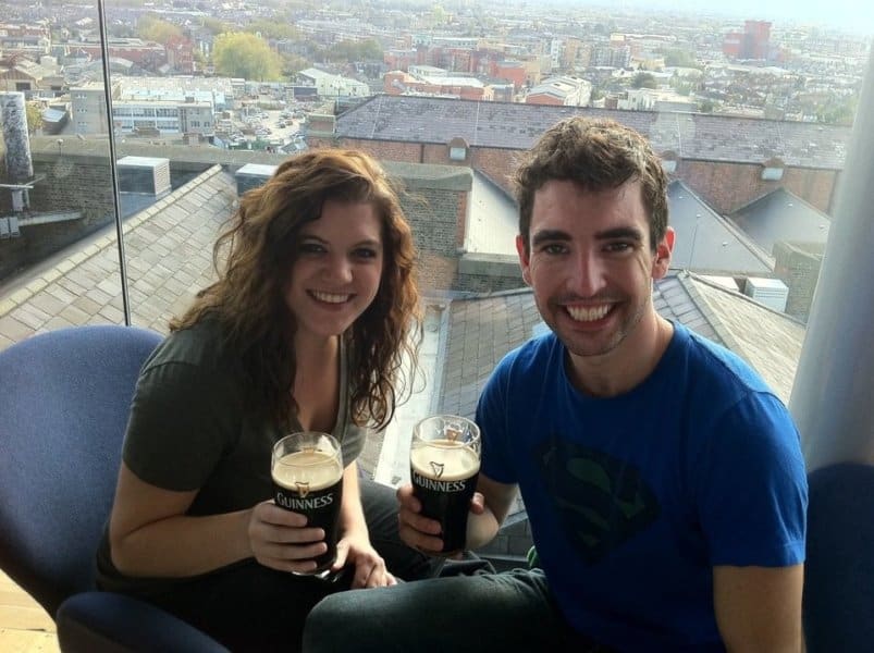 A woman and man sit next to each other smiling while holding pints of Guinness.