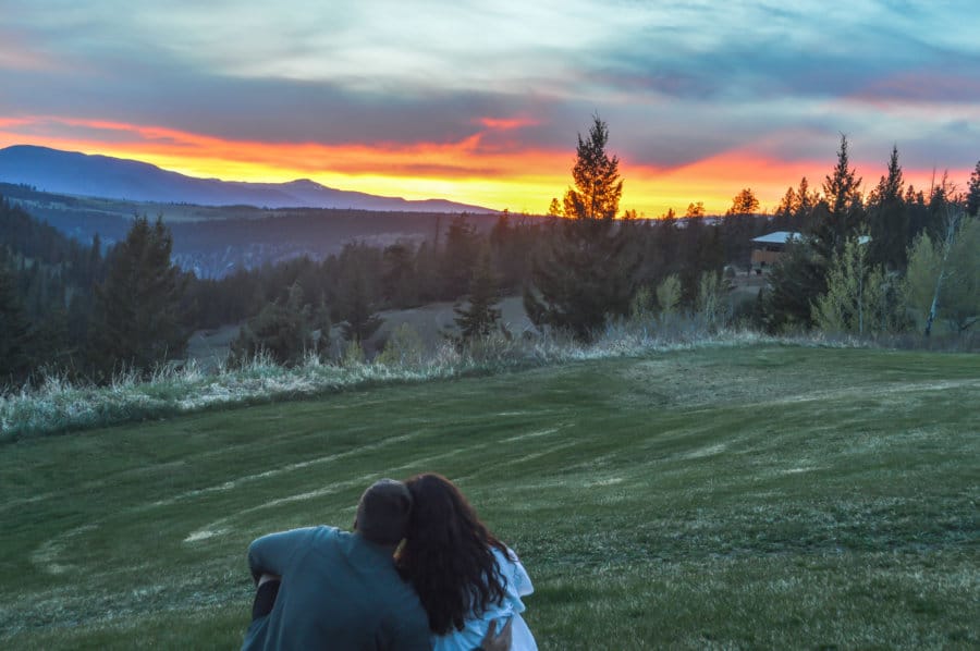 A couple embraces one another while looking out at mountains as the sun sets.