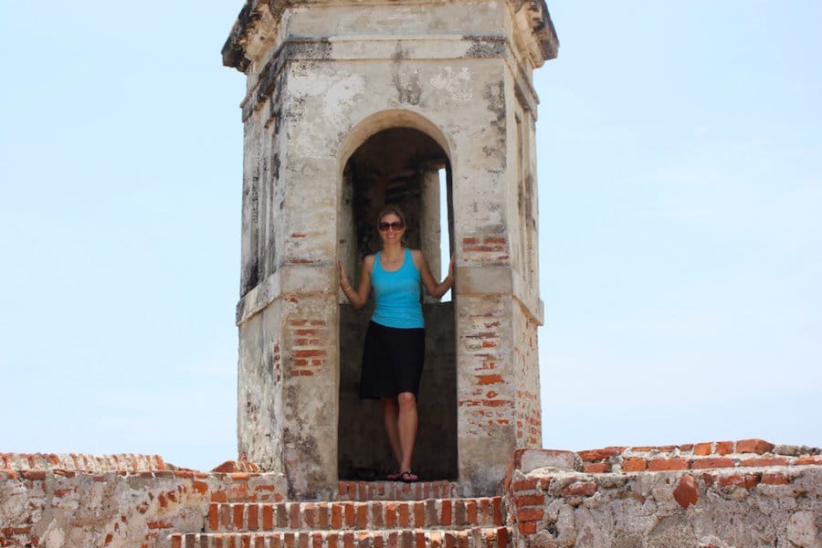 Woman stands in an arched doorway at the top of stairs.