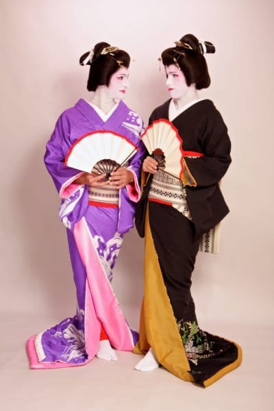 Two people smile in geisha outfits.