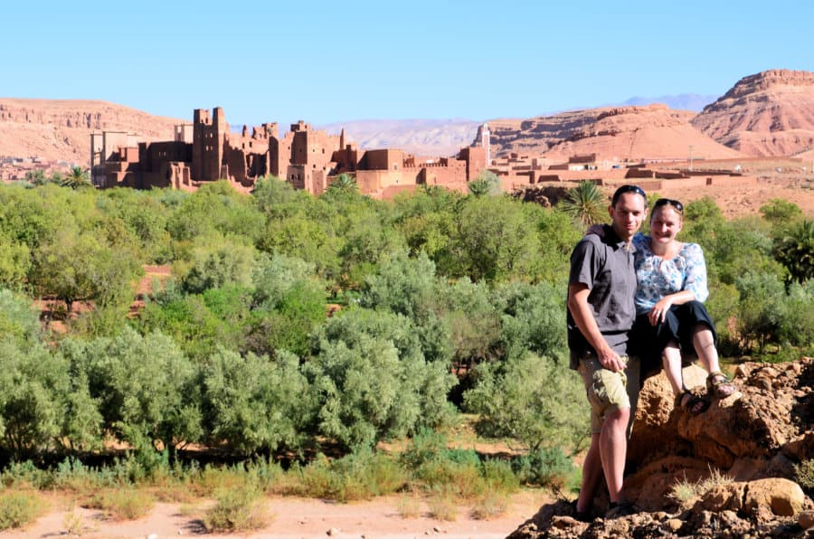 A couple smiles with ancient ruins behind them.