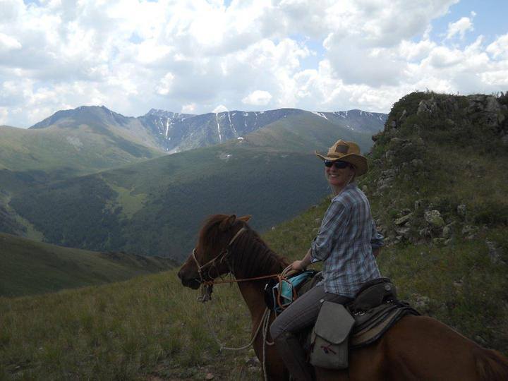 A woman rides a horse looking out to the mountains.