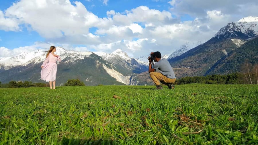 A man is crouched on a grassy hill with his camera, taking a picture.