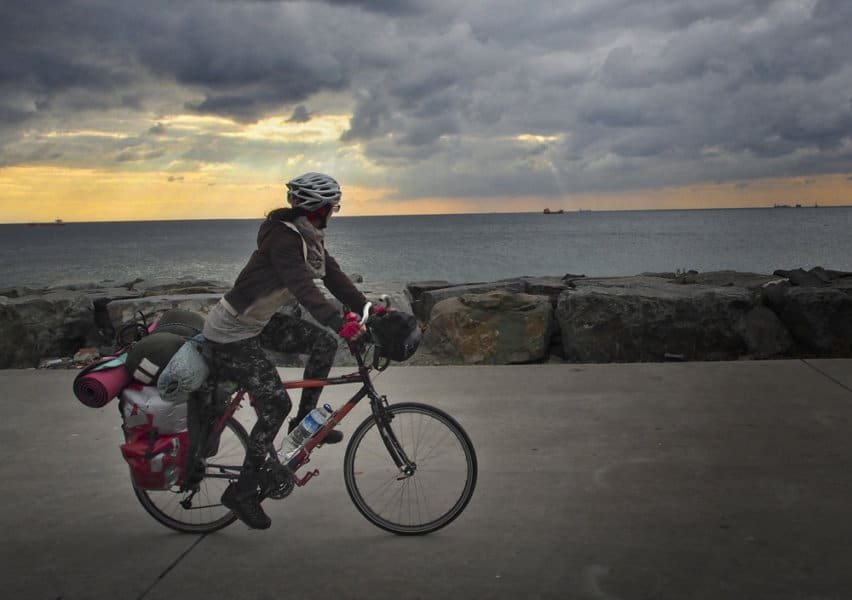 A person rides the bike next to the ocean under a sunset sky.