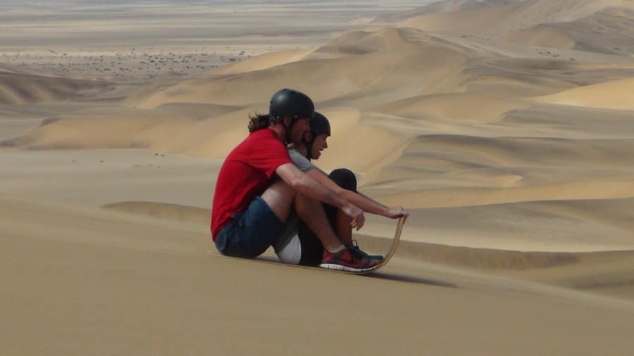 Two people sled down a sand dune.