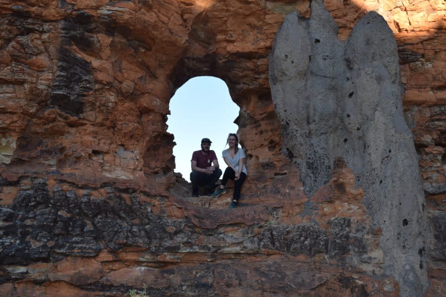 A couple sits inside an arched rock.