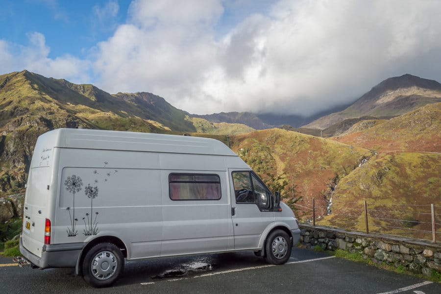A white van is parked in a parking spot surrounded by mountains.