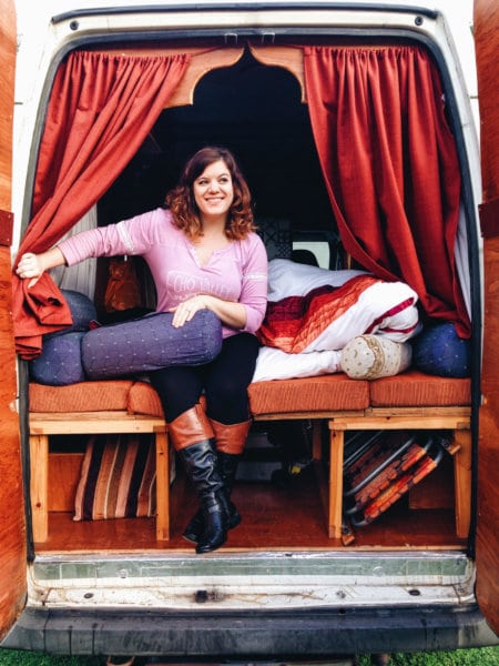 A woman smiles while sitting in the back of a campervan.