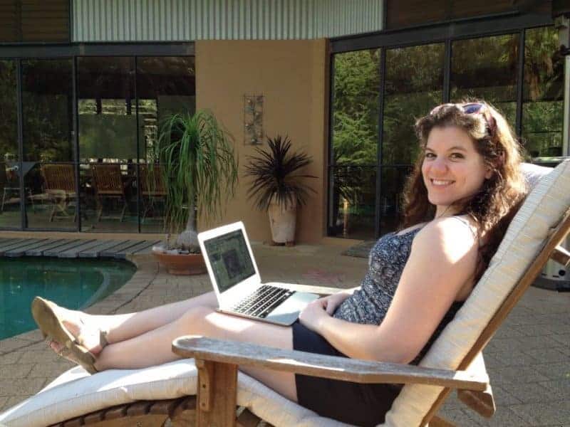 A woman sits near the pool while working on her laptop.
