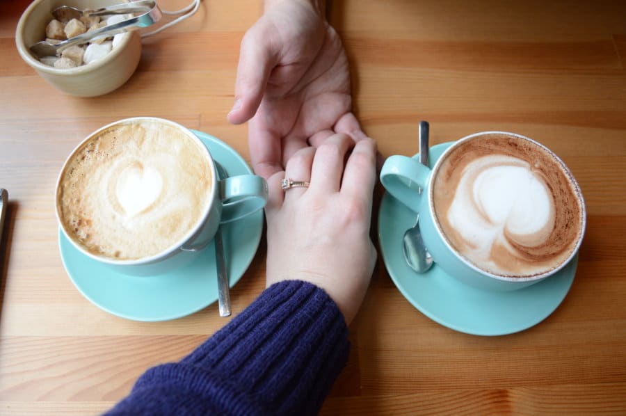 A couple holds hands with blue cups of coffee on either side of them.