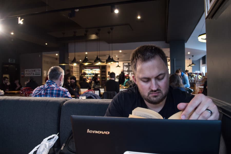 A man reads a book with a laptop open.