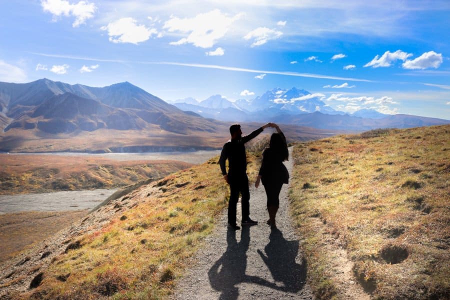 A couple walks on a walkway with mountains behind them.