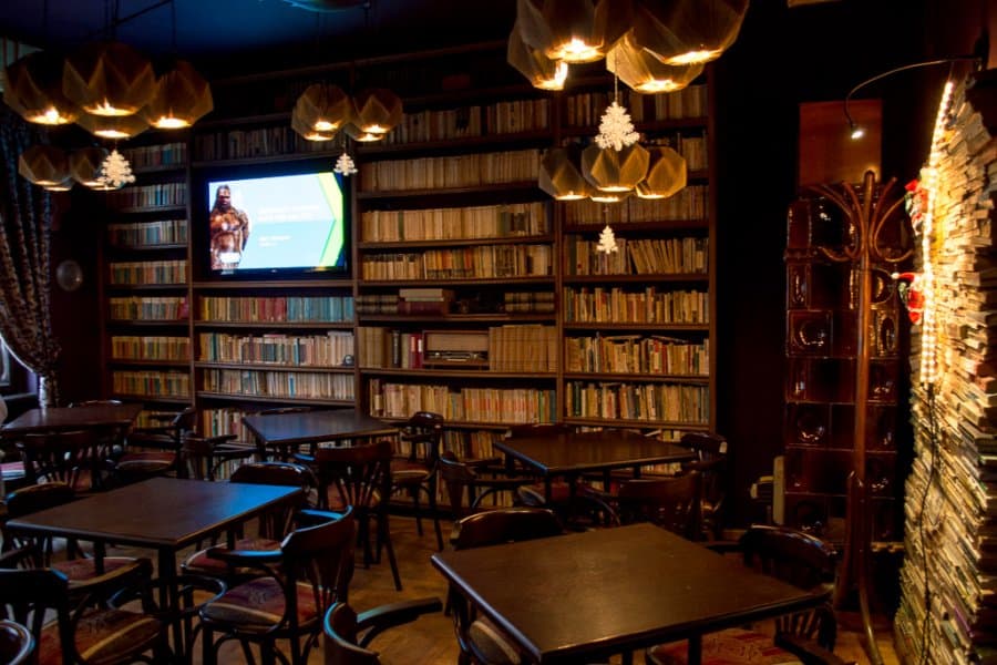 Tables and chairs in a cafe filled to the brim with bookshelves.