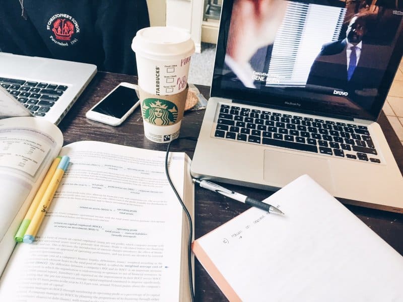 A white Starbucks cup next to a laptop and books open.