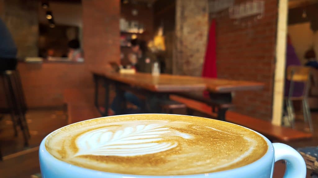 Close up of latte art in a blue mug. A cafe is blurred out behind it.