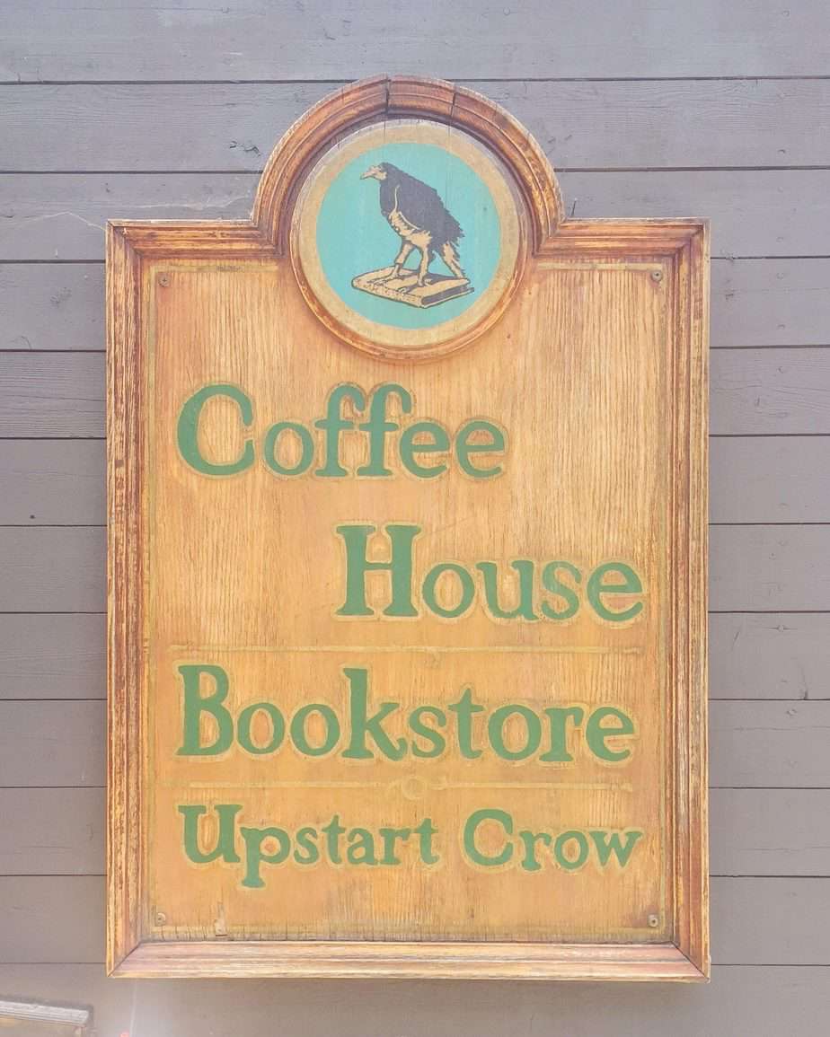 A wooden sign that says "Coffee House Bookstore Upstart Crow."