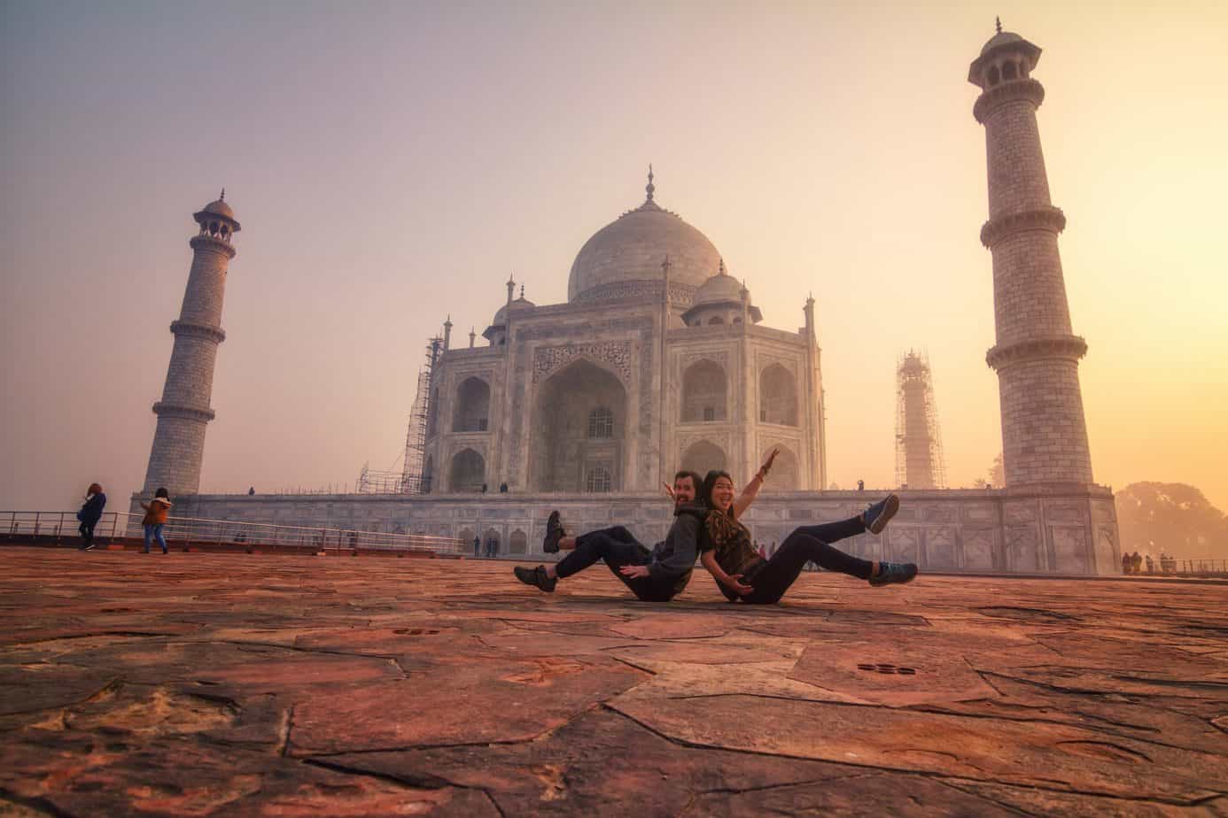 A couple sits back to back in front of Taj Mahal