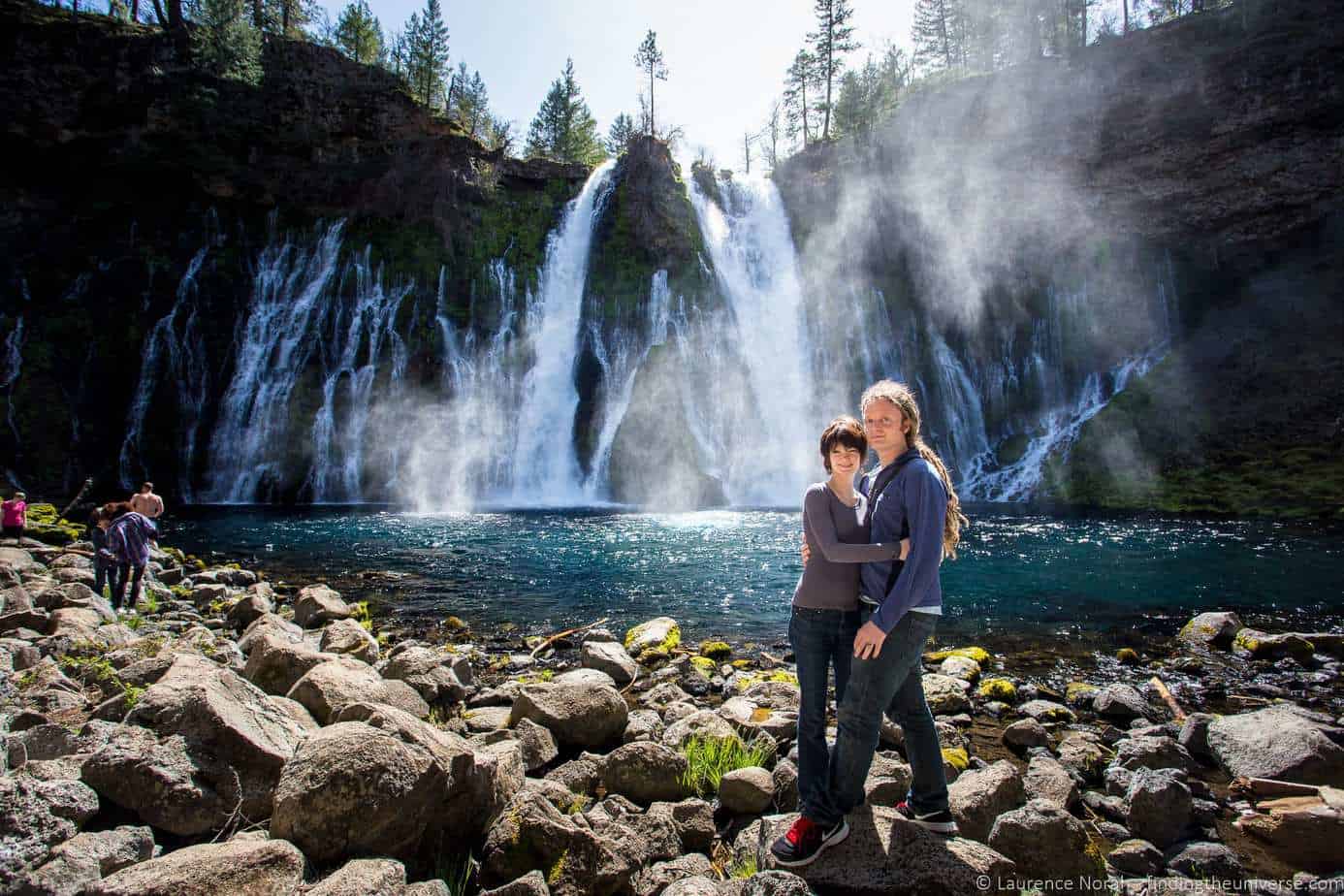 A couple poses in front of a giant waterfall