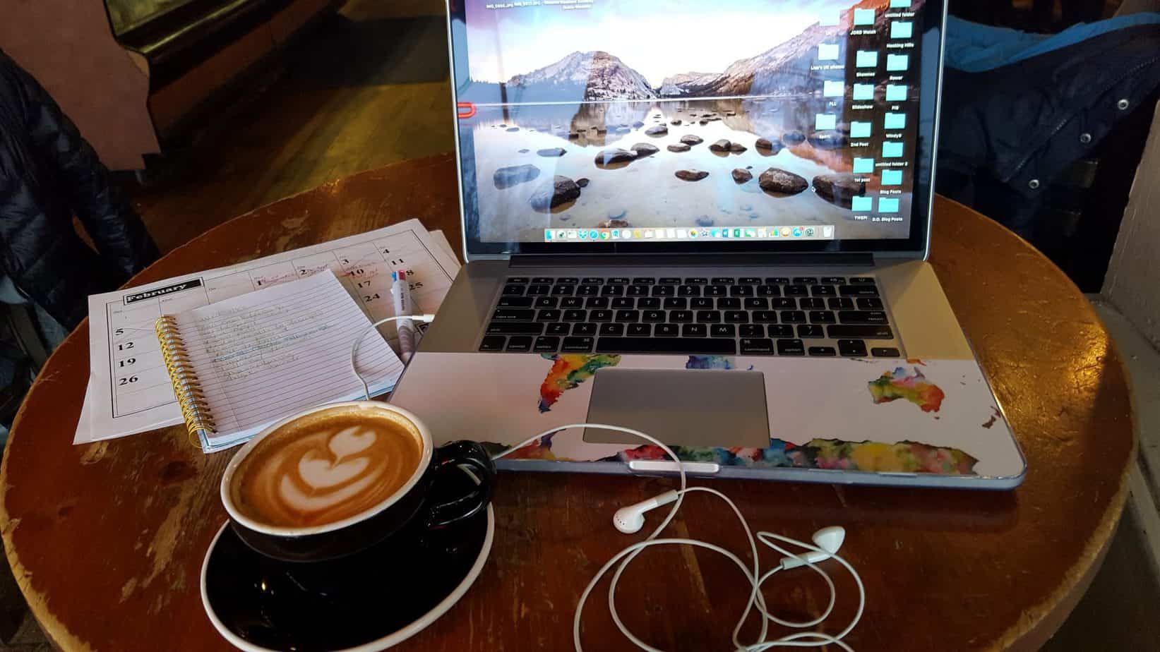 A cup of coffee sits next to a journal and a laptop.