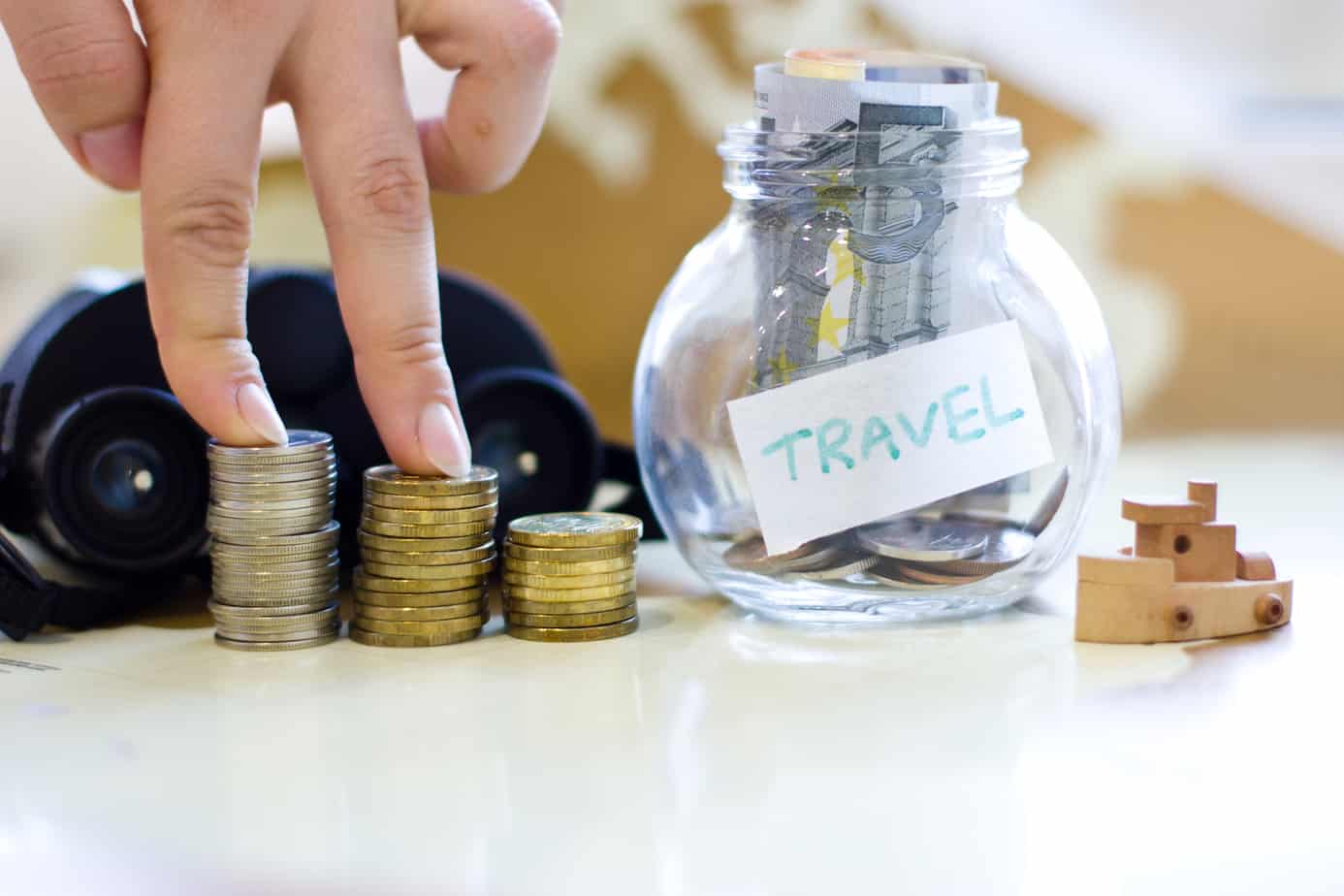 A person's hands are on money next to a money jar that says Travel