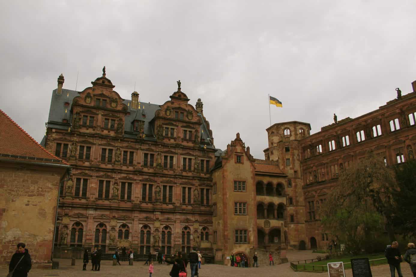 People walk around a square next to tall brick buildings with a flag.