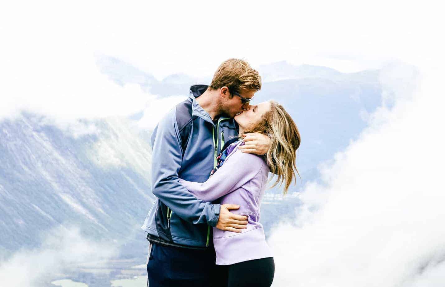 A couple kisses with a view of a mountain behind them.