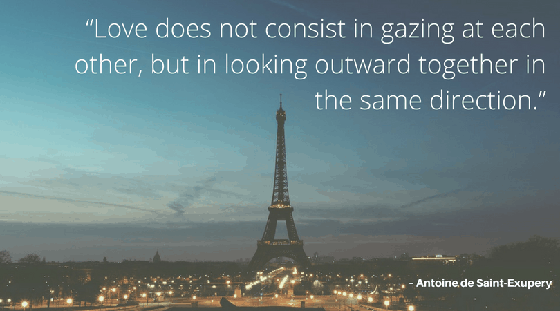 Image of the Eiffel Tower with text that says \"Love does not consist in gazing at each other, but in looking outwards together in the same direction.\" - Antoine de Saint-Exupery