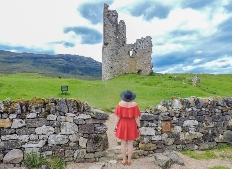 A girl in a red dress looks out at a stone castle.