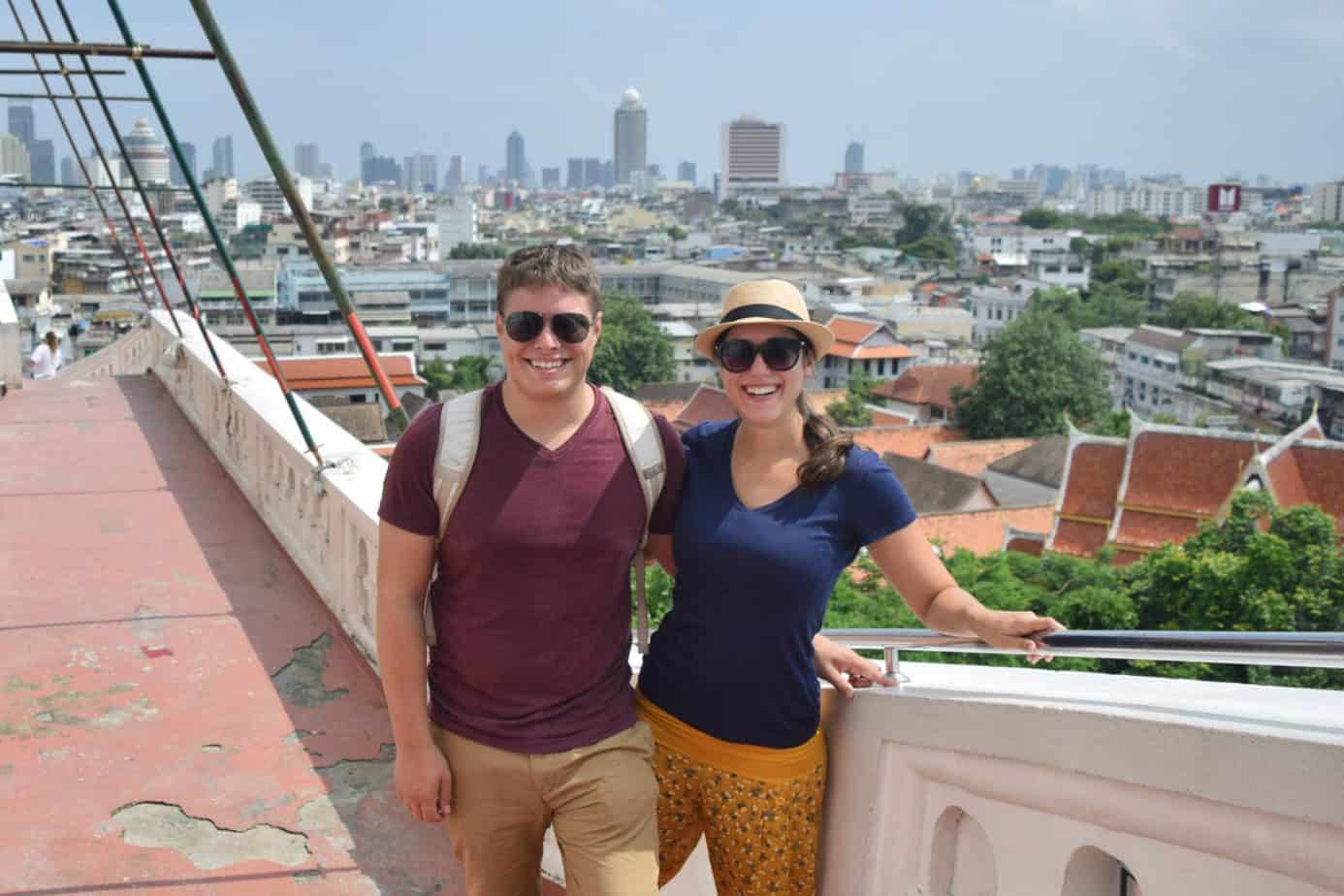 A couple holds one another and poses with a city skyline behind them.