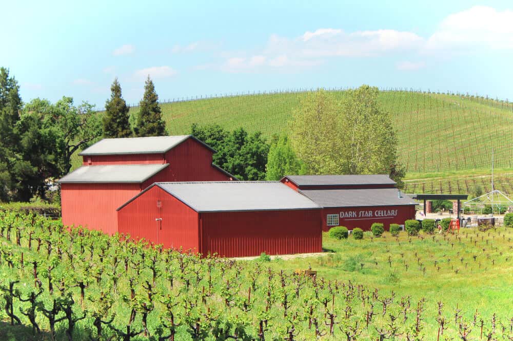 Big red farm buildings that say \"Dark Star Cellars\" surrounded by vineyards.
