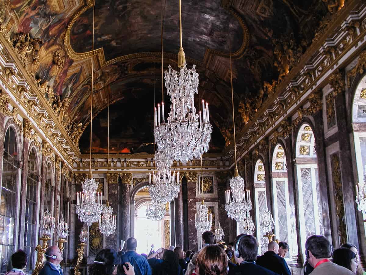 Interior of a long building with chandeliers as people walk around with cameras.