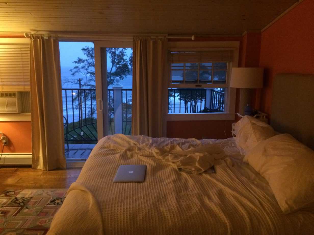 A bedroom with a bed and a window. A laptop sits on the bed.
