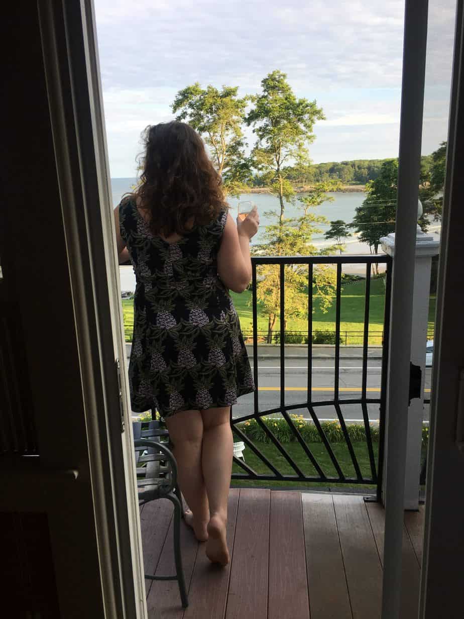 A woman in a black dress looks out from a balcony at the water.