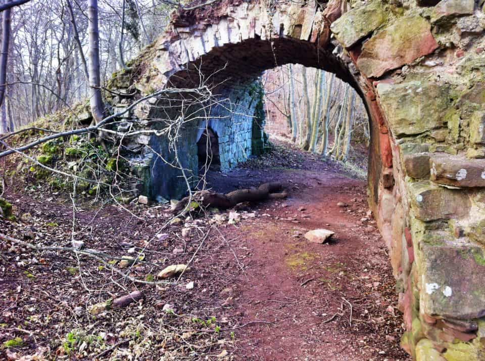 A path in a forest leading under a stone bridge.