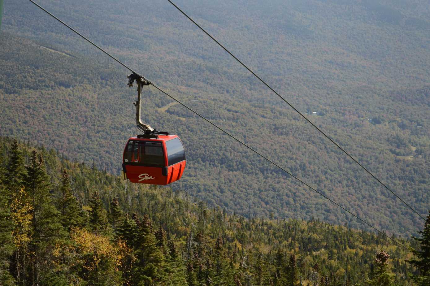 A red cable car lifts people high up in the mountains.