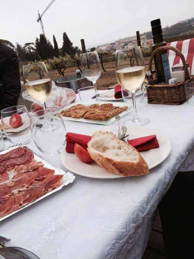 A white table is set with meats and cheese and glasses of wine.