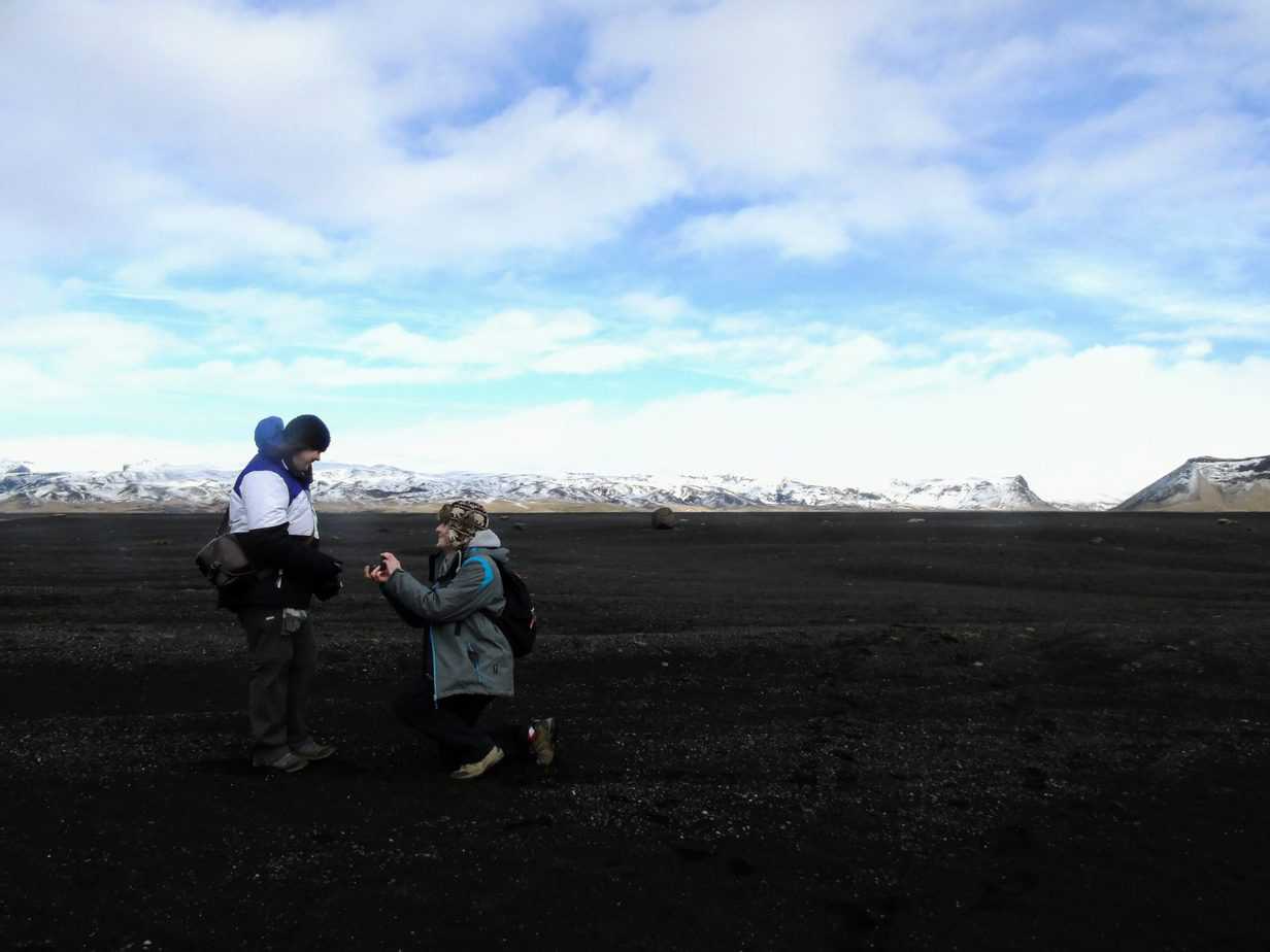 Someone leans down and proposes to their partner with snowy mountains in the background.