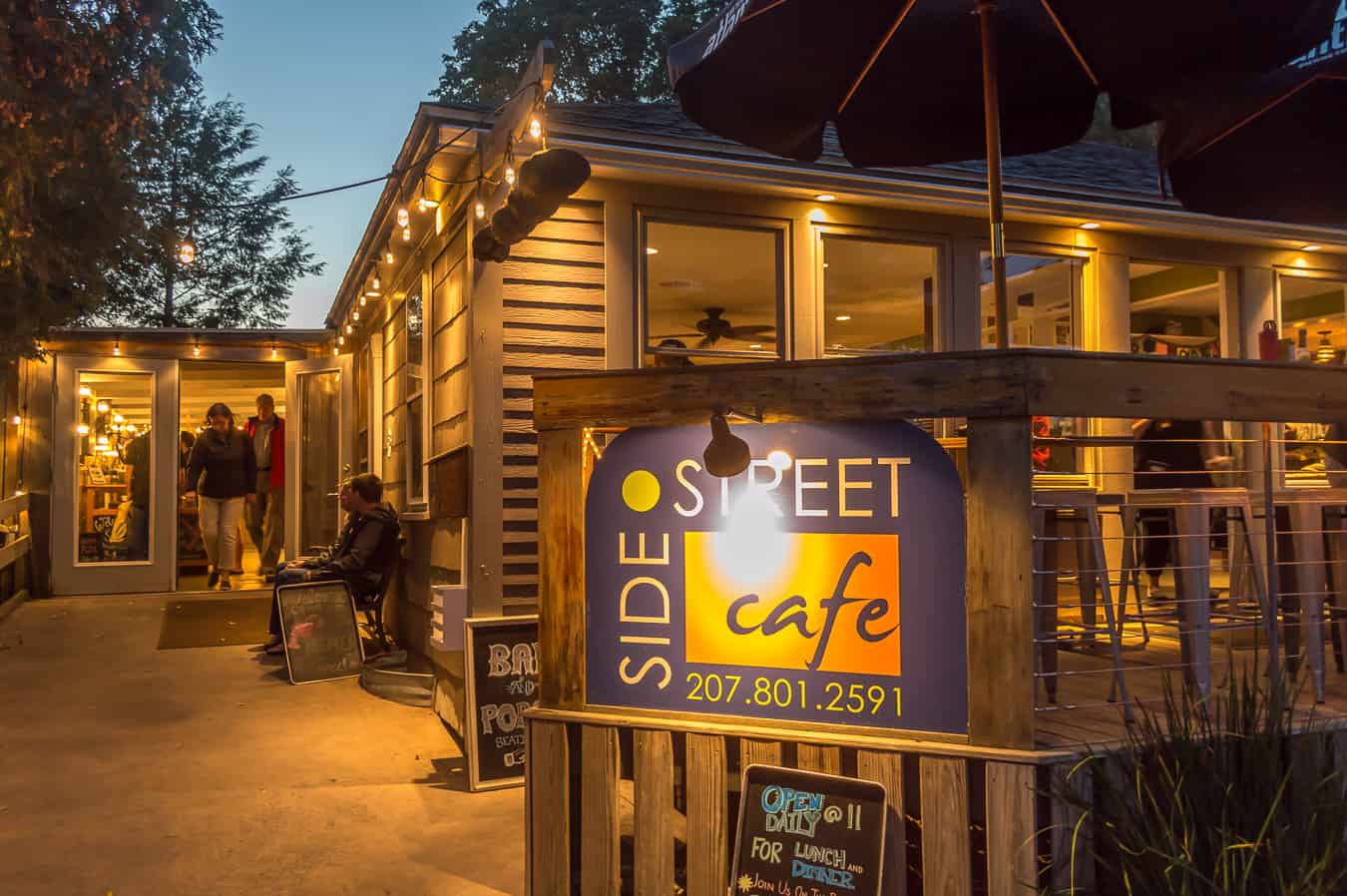 Blue and orange sign that says Side Street Cafe, with the cafe in the background under a dark blue sky in Bar Harbor Maine.