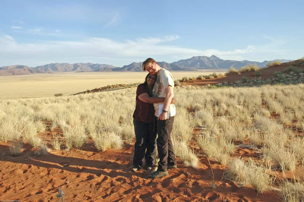 A couple holds each other in a desert with mountains behind.