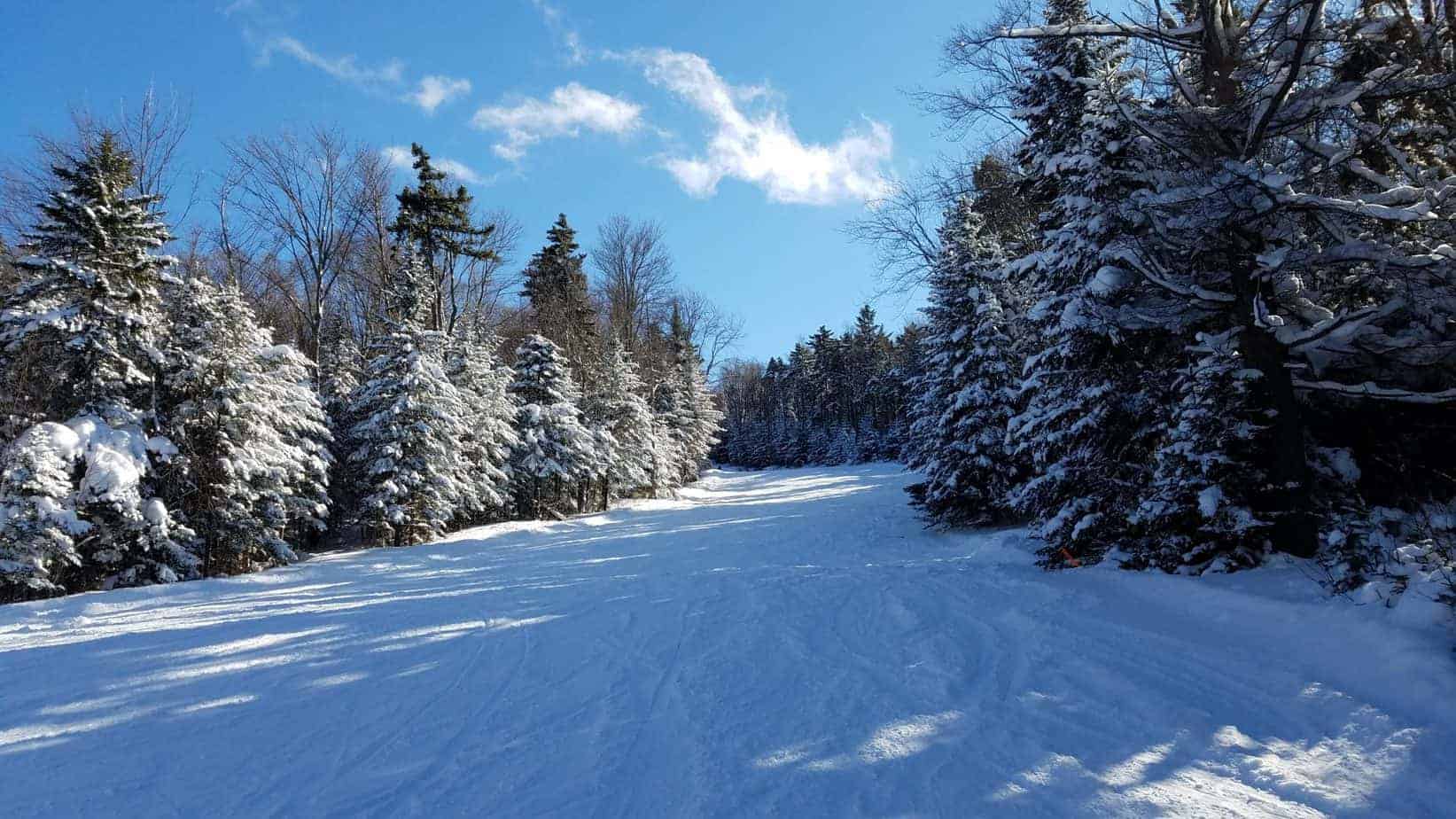 Empty ski run at a ski resort covered in snow on a blue sunny day.