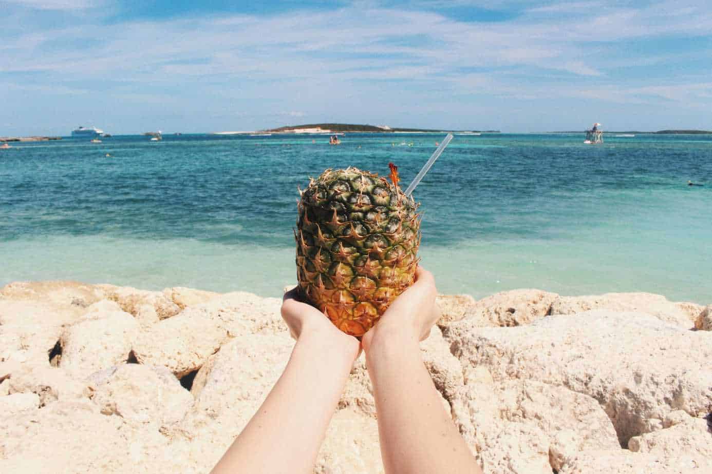 A person holds a pineapple drink with the ocean behind them.