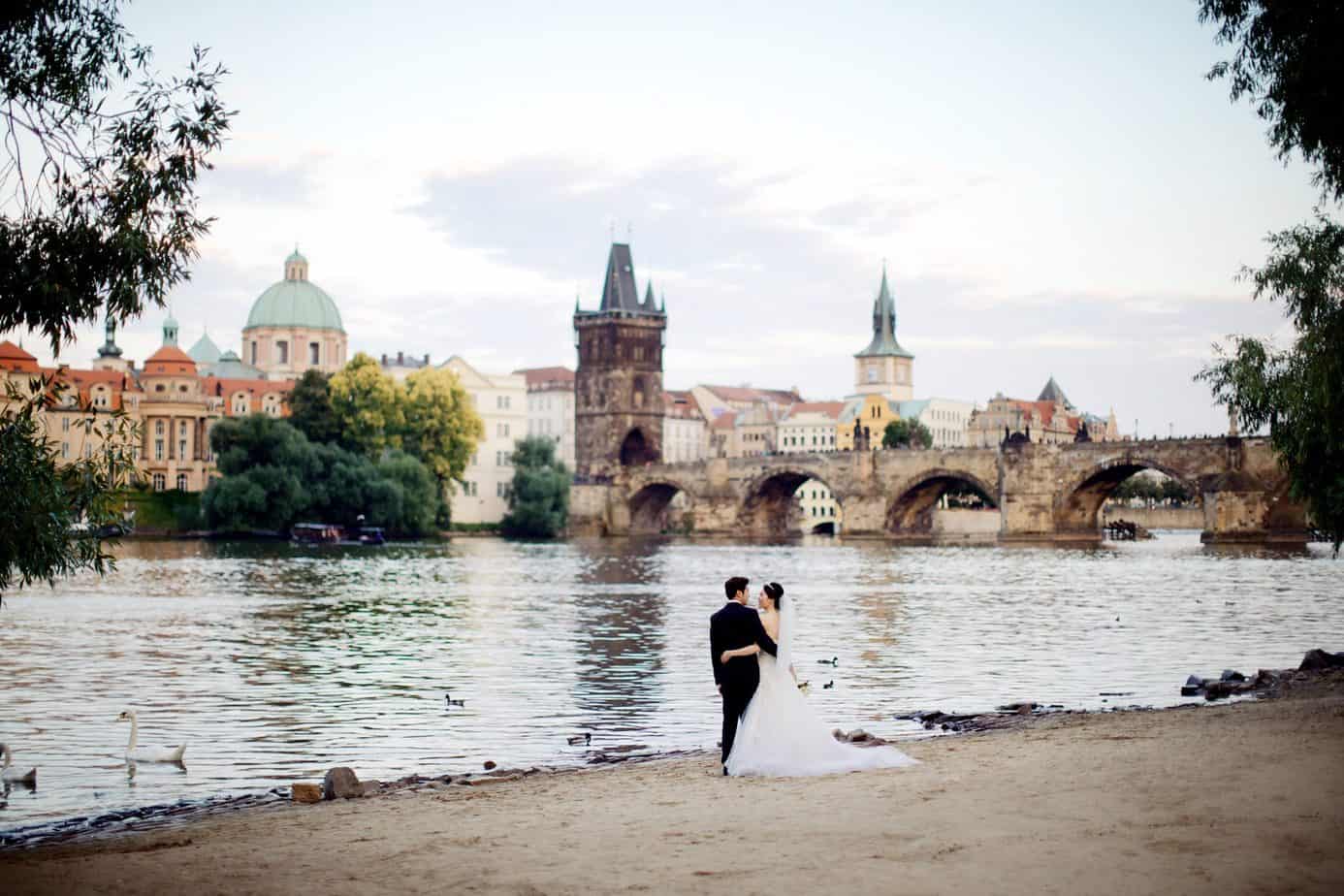 A couple in wedding clothing next to the water. A city skyline is in the back.