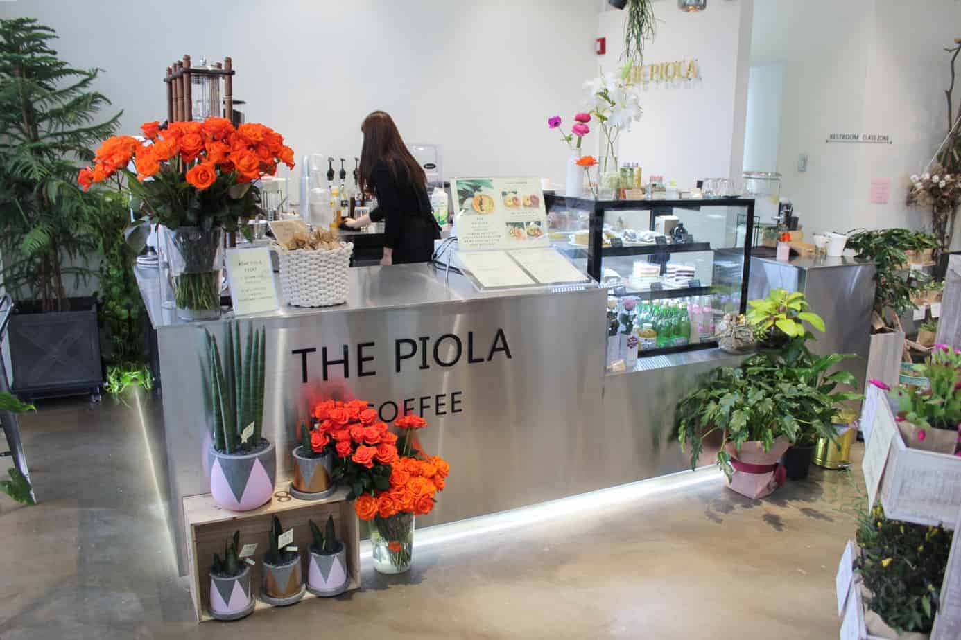 Barista working behind a silver counter that says The Piola Coffee.