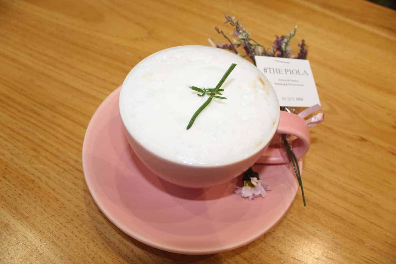 Pink mug with a drink in it next to flowers.