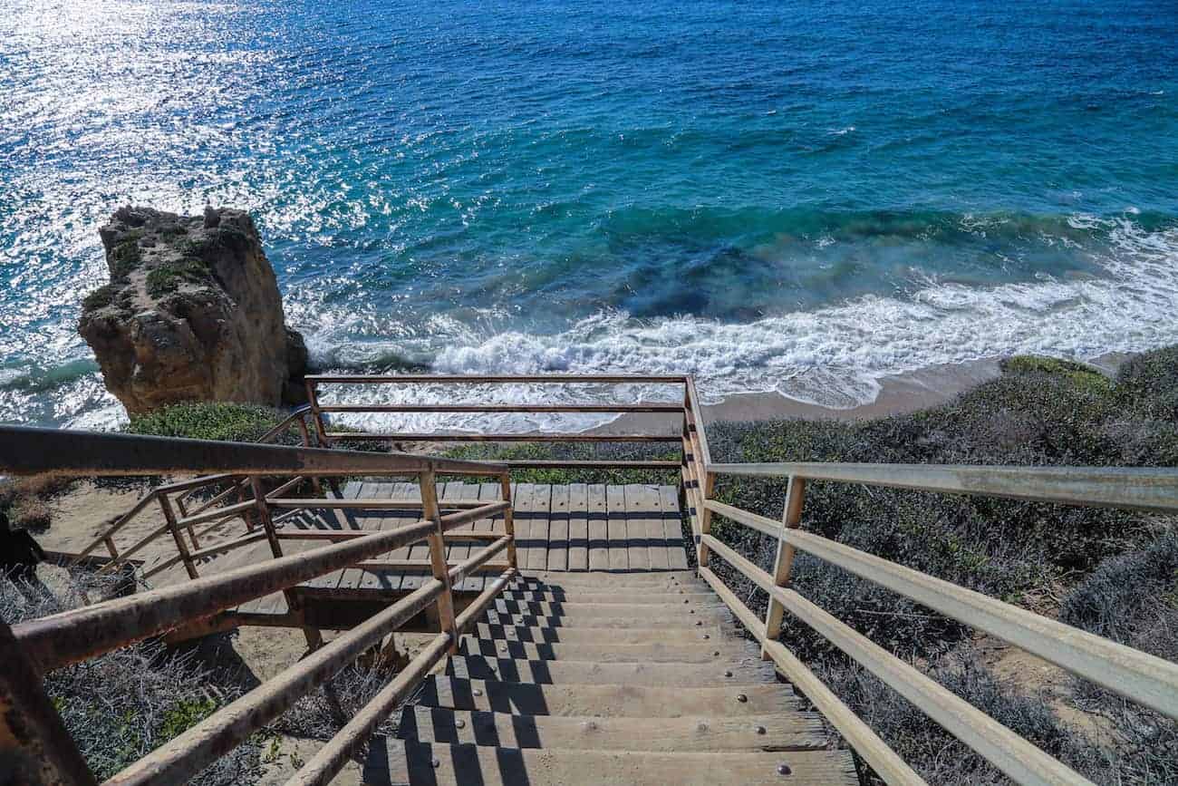 A wooden walkway leads down to a view of a blue beach.