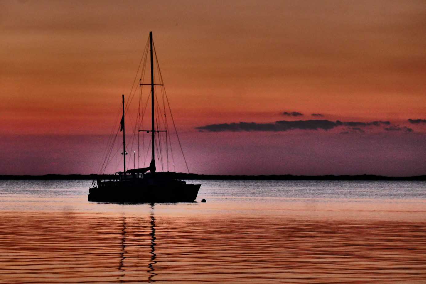 A sailboat floats on the water under a red and pink sky.