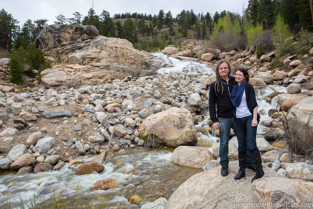 Two people standing on a rock next to a small river. 