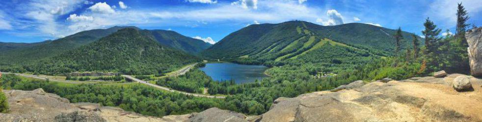 A large blue lake at the bottom of a grassy mountain range. 