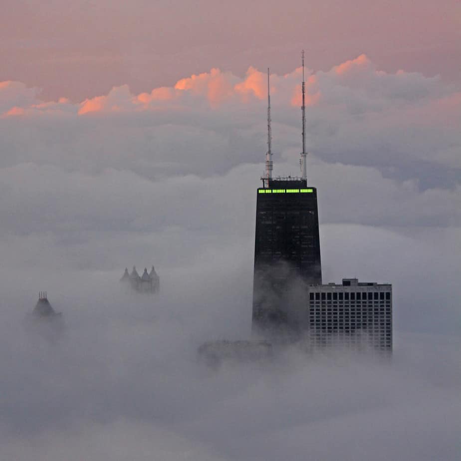 The tops of skyscrapers cutting through the clouds at sunset. 