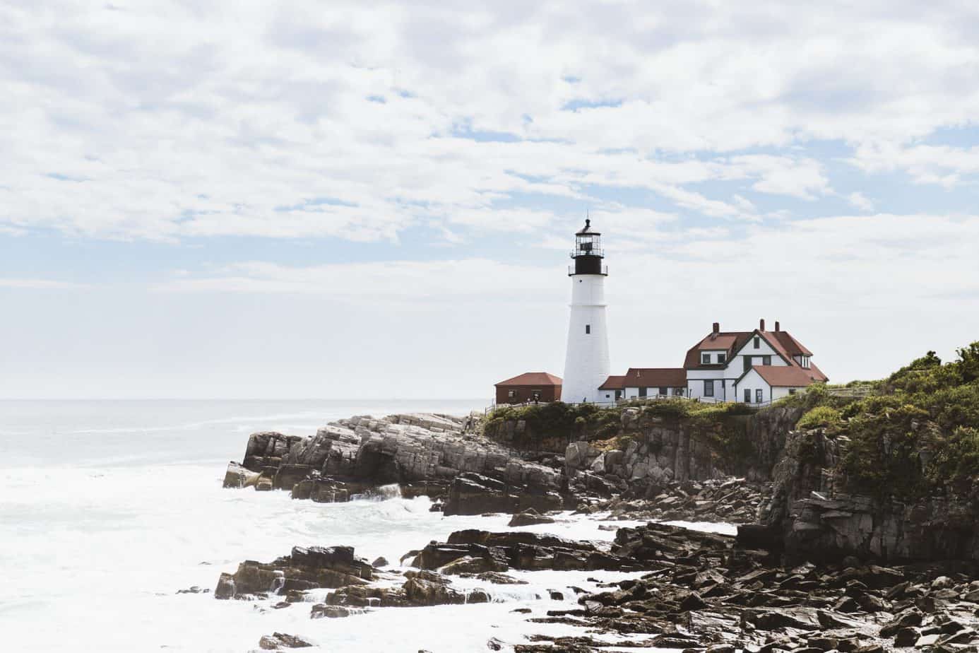 A white lighthouse with a house next to it on rocks along the edge of the water